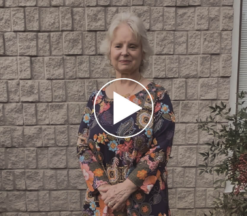 Brenda standing outside of Faith Temple Church and a play video button