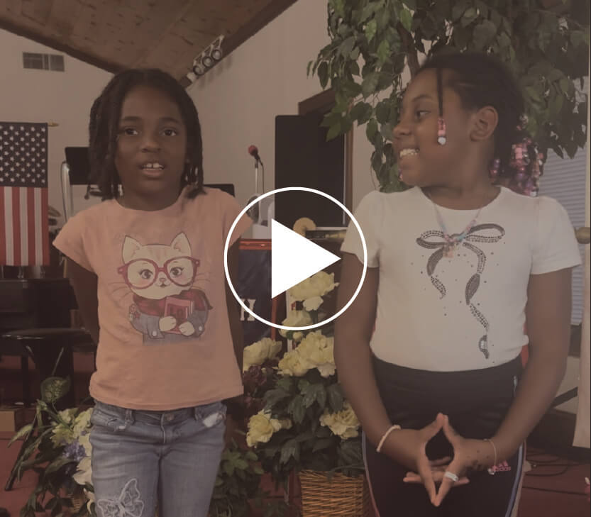 Two young girls standing in Faith Temple Church and a video play button