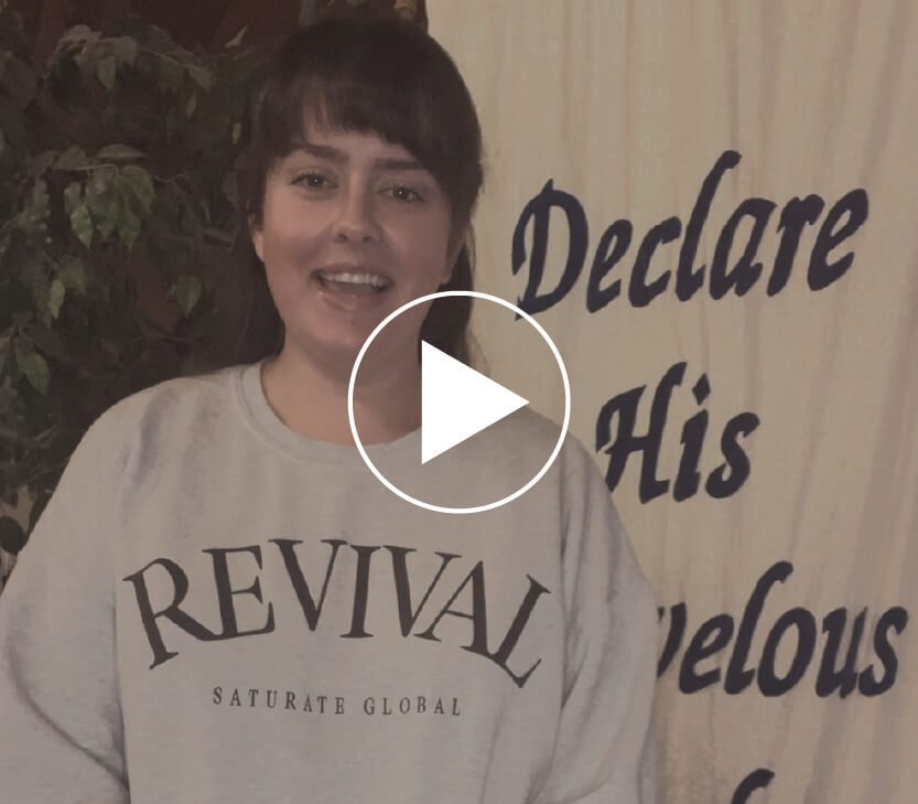 Olivia standing in front of a banner that says Declare His marvelous works and a video play button